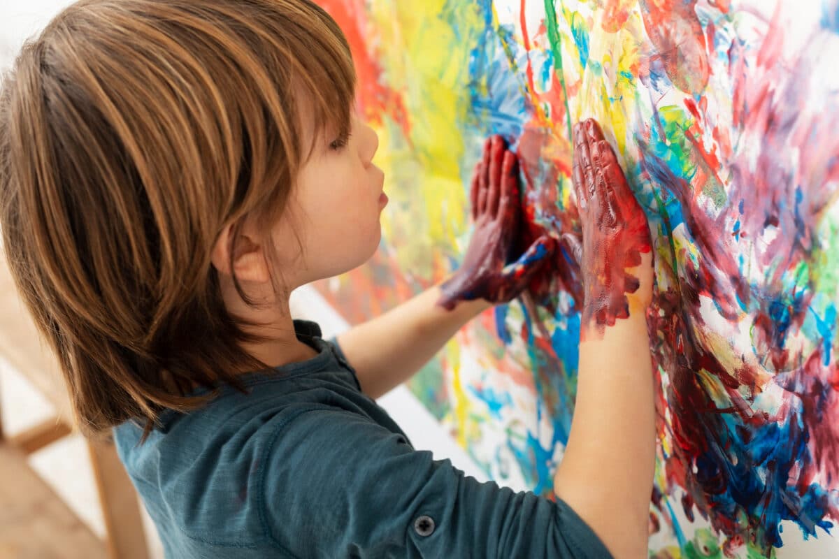 La liberté de créer en se salissant : un enfant plongeant ses mains dans la peinture, illustrant la joie de l’exploration artistique dans un atelier dédié à l’expression libre