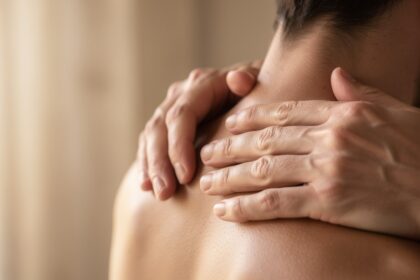 Mains posées sur la nuque pour un automassage à la lumière naturelle d'une fenêtre.