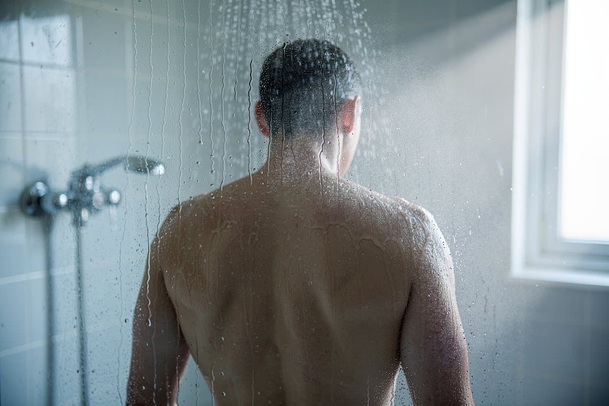 Personne sous une douche dans une salle de bain, lumière naturelle douce, gouttelettes d'eau