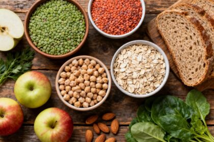 Aliments riches en fibres sur une table en bois : legumineuses, flocons d'avoine, pain complet, pommes et amandes.