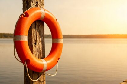 Bouée de sauvetage orange accrochée à un poteau en bois au bord d'un plan d'eau calme sous le soleil d'été