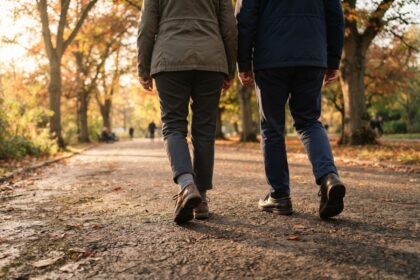 Deux personnes marchent de dos sur une allée de parc en automne, cadrées sur les jambes et les pas