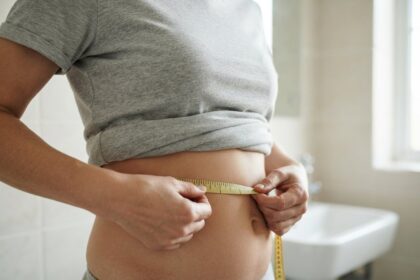 Une femme mesure son tour de taille avec un mètre ruban souple, dans une salle de bains claire